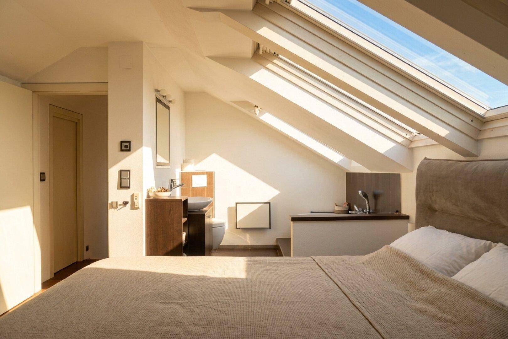 Schlafzimmer im Dachgeschoss mit integriertem Badbereich und hellen Dachfenstern.