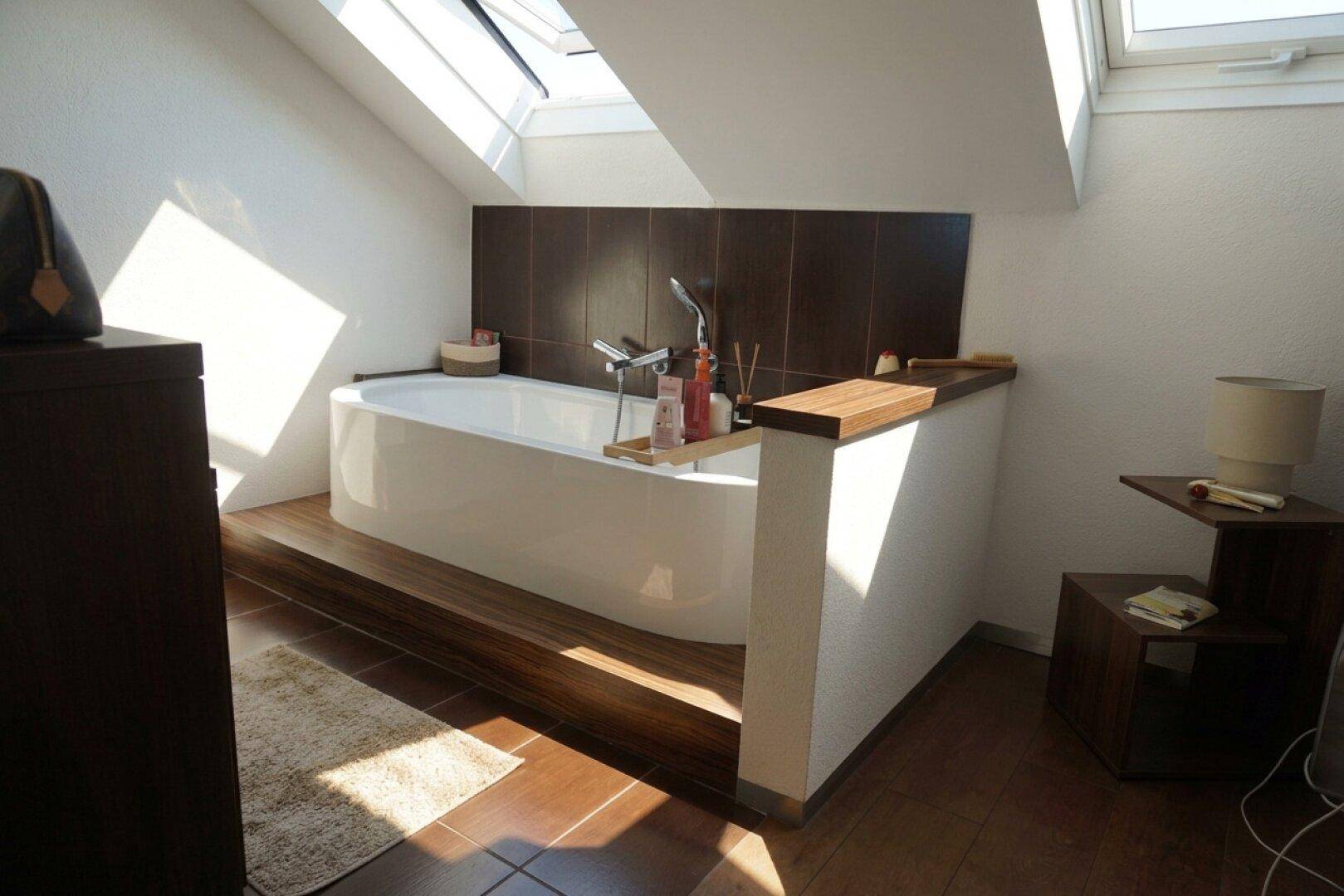 Modernes Badezimmer mit Badewanne und Holzboden unter der Dachschräge.