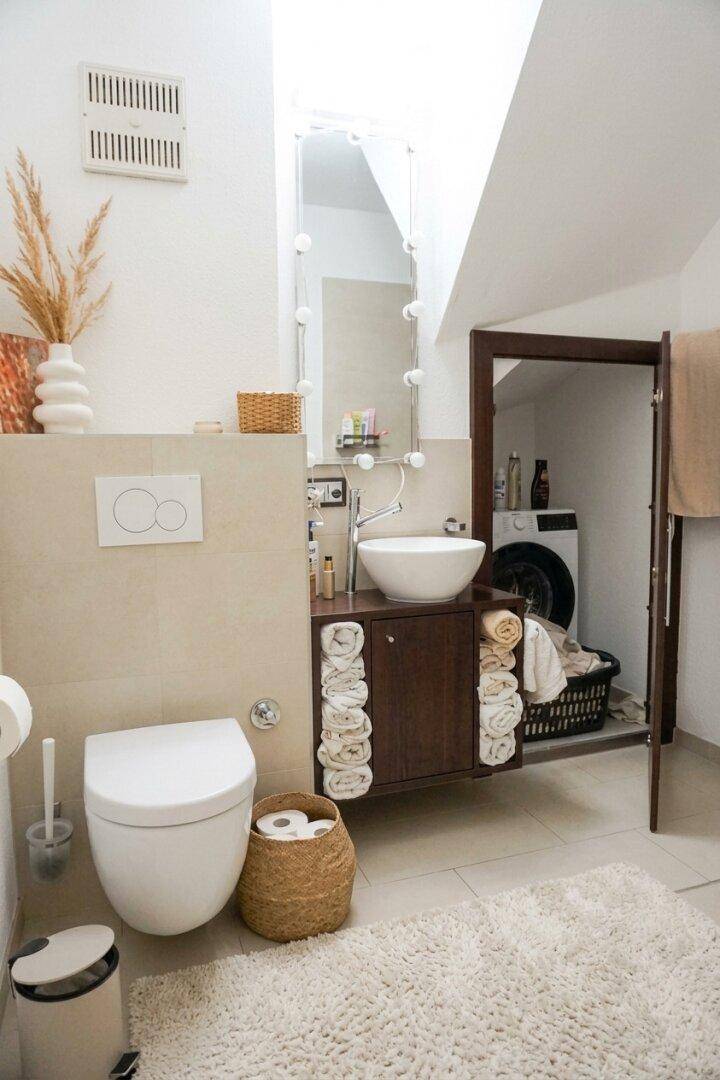 Badezimmer mit Waschtisch, Toilette und integriertem Waschmaschinenbereich unter der Dachschräge.