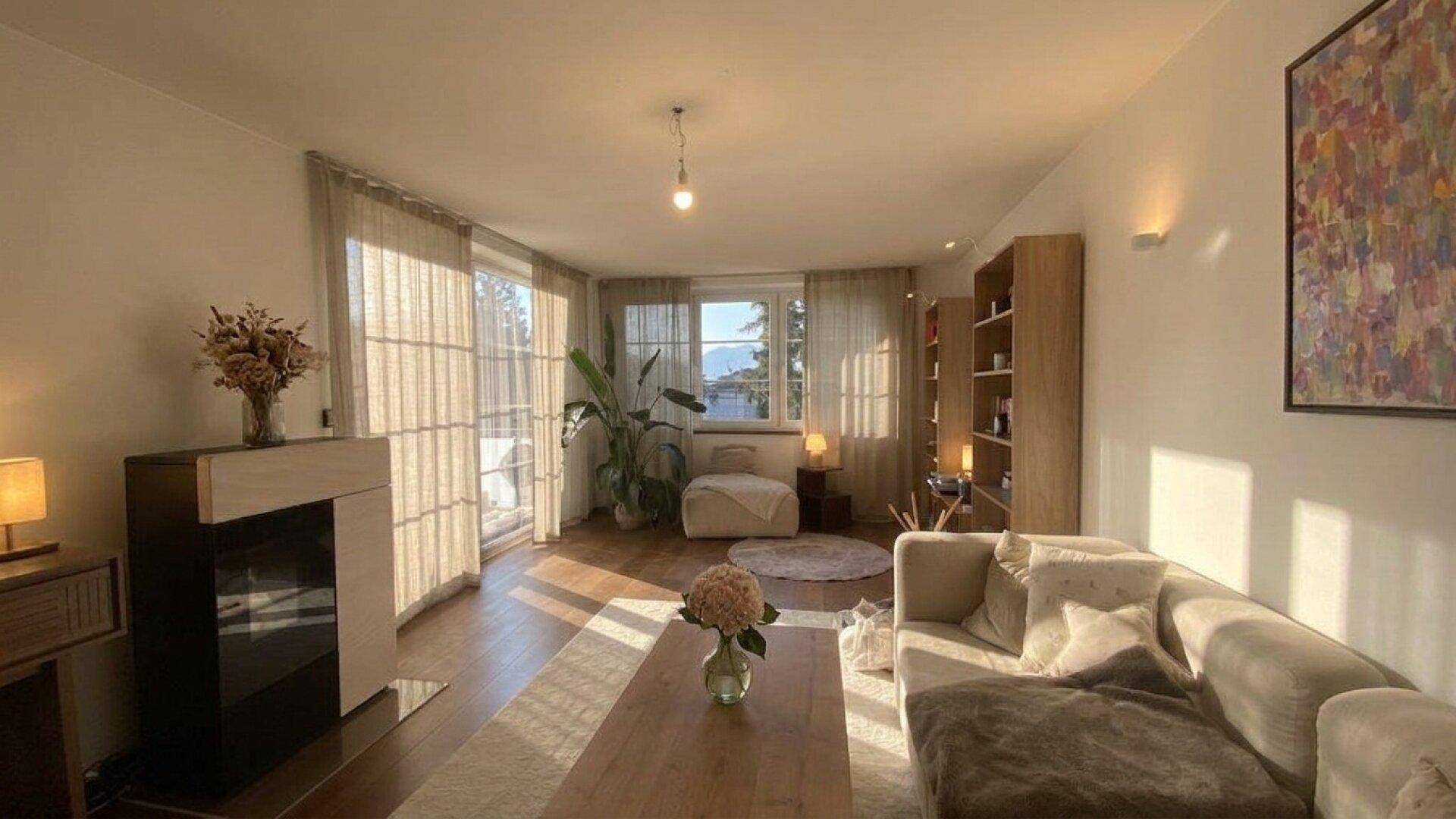 Gemütliches Wohnzimmer mit Kamin, Holzboden und viel Tageslicht durch große Fenster.