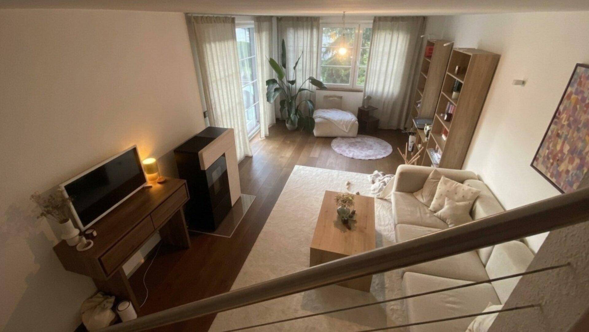 Geräumiges Wohnzimmer von oben betrachtet, mit Kamin und Zugang zur Terrasse.