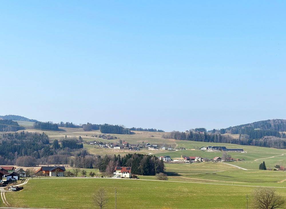Idyllische Landschaft mit sanften grünen Hügeln, verstreuten Häusern und Wäldern in der Ferne.