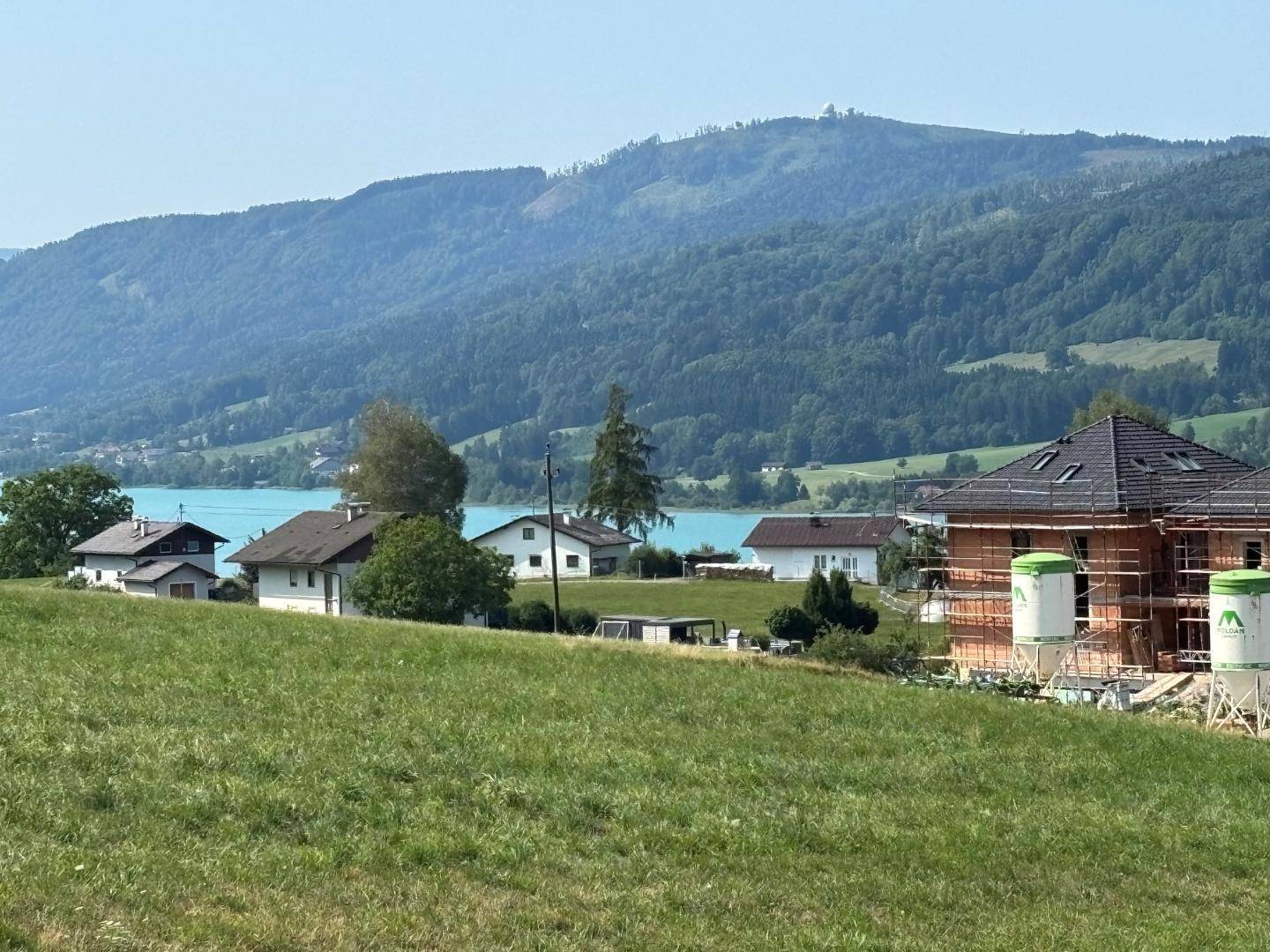 Häuser mit Seeblick und Bergblick, teilweise im Bau, umgeben von grünen Hügeln.