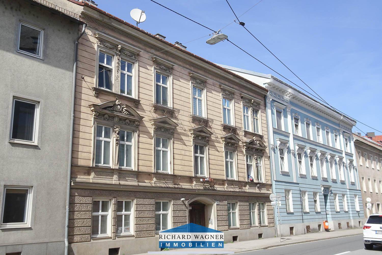 Historisches Wohngebäude an einer Straße, umgeben von weiteren Altbauten mit klassischer Fassade.
