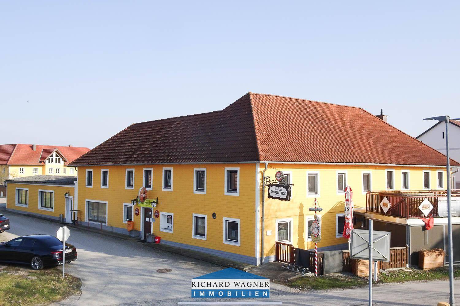 Weitläufige Ansicht des gelben Gasthauses mit rotem Dach und angrenzenden Gebäuden in ländlicher Umgebung.