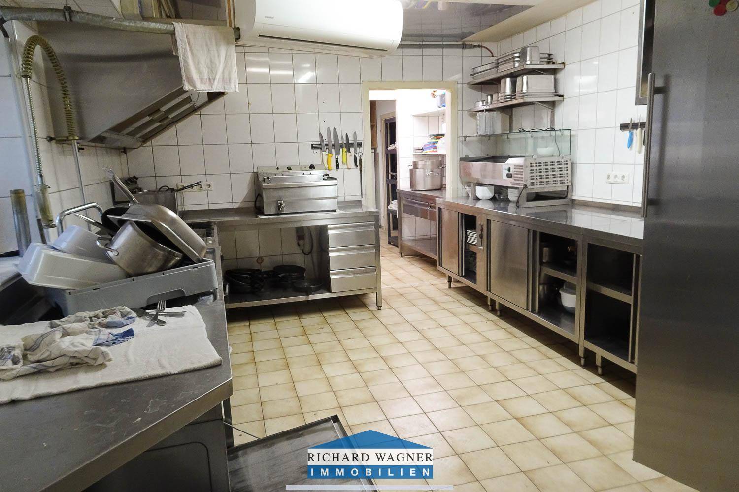 Professionelle Großküche mit Edelstahlgeräten, Fliesenboden und Abluftanlage für den Gastronomiebetrieb.