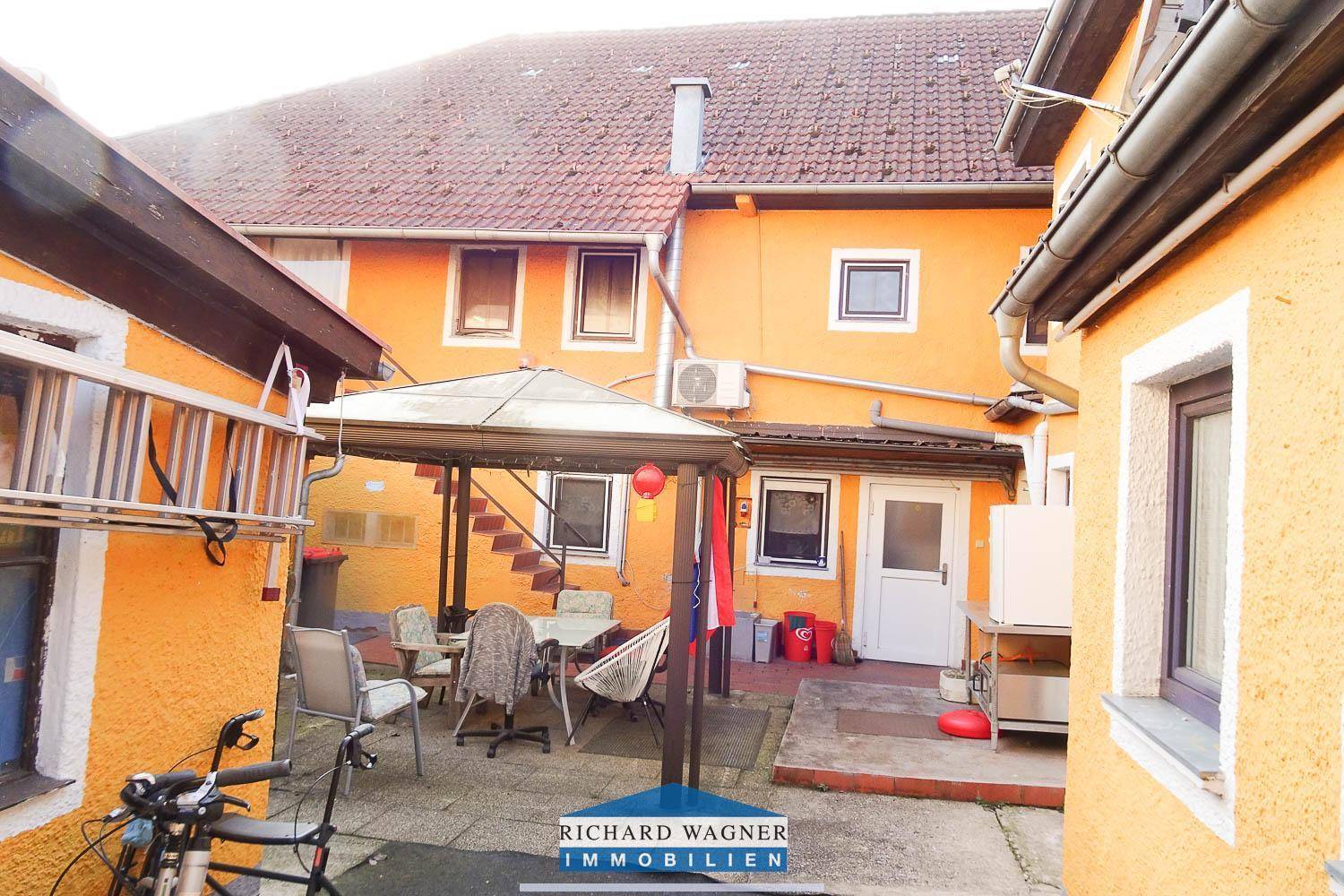 Gemütlicher Innenhof mit überdachtem Sitzbereich, umgeben von den gelb-orangen Gebäudewänden.