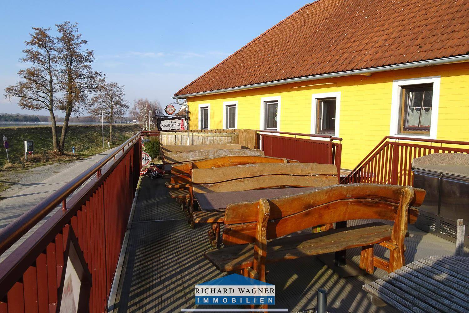 Große Außenterrasse mit rustikalen Holzbänken und Blick auf die umliegende Landschaft und das Wasser.