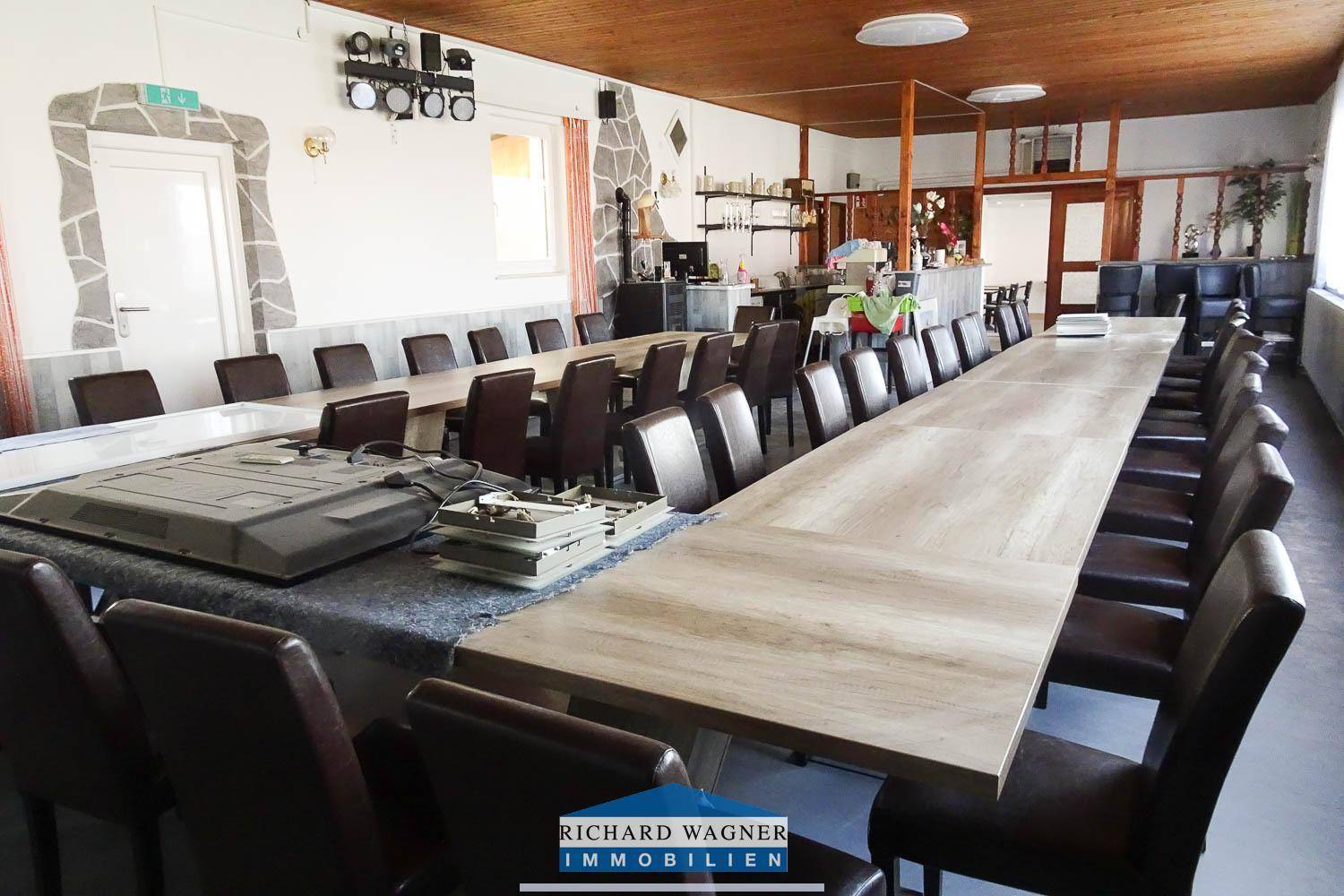 Großer Speisesaal oder Veranstaltungsraum mit langen Tischen, vielen Stühlen und Holzdeckenverkleidung.