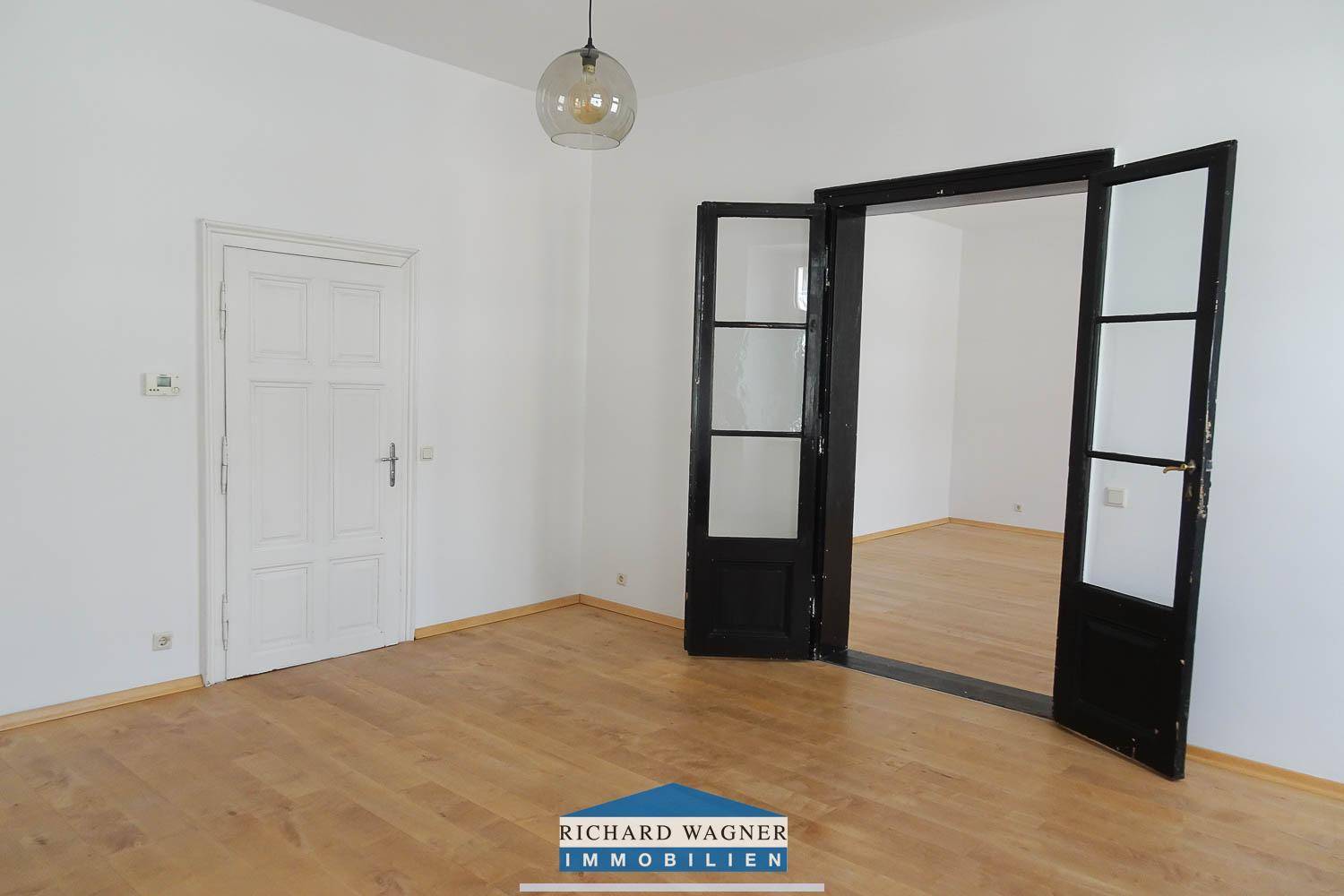 Helles Zimmer mit Holzboden und einer klassischen weißen Tür, die zu einem weiteren Raum führt und Privatsphäre bietet.