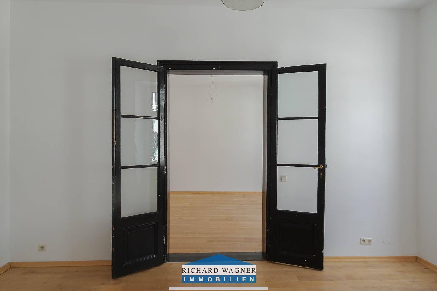 Leeres Zimmer mit Holzboden und eleganten Flügeltüren, bereit zur individuellen Gestaltung und Nutzung.