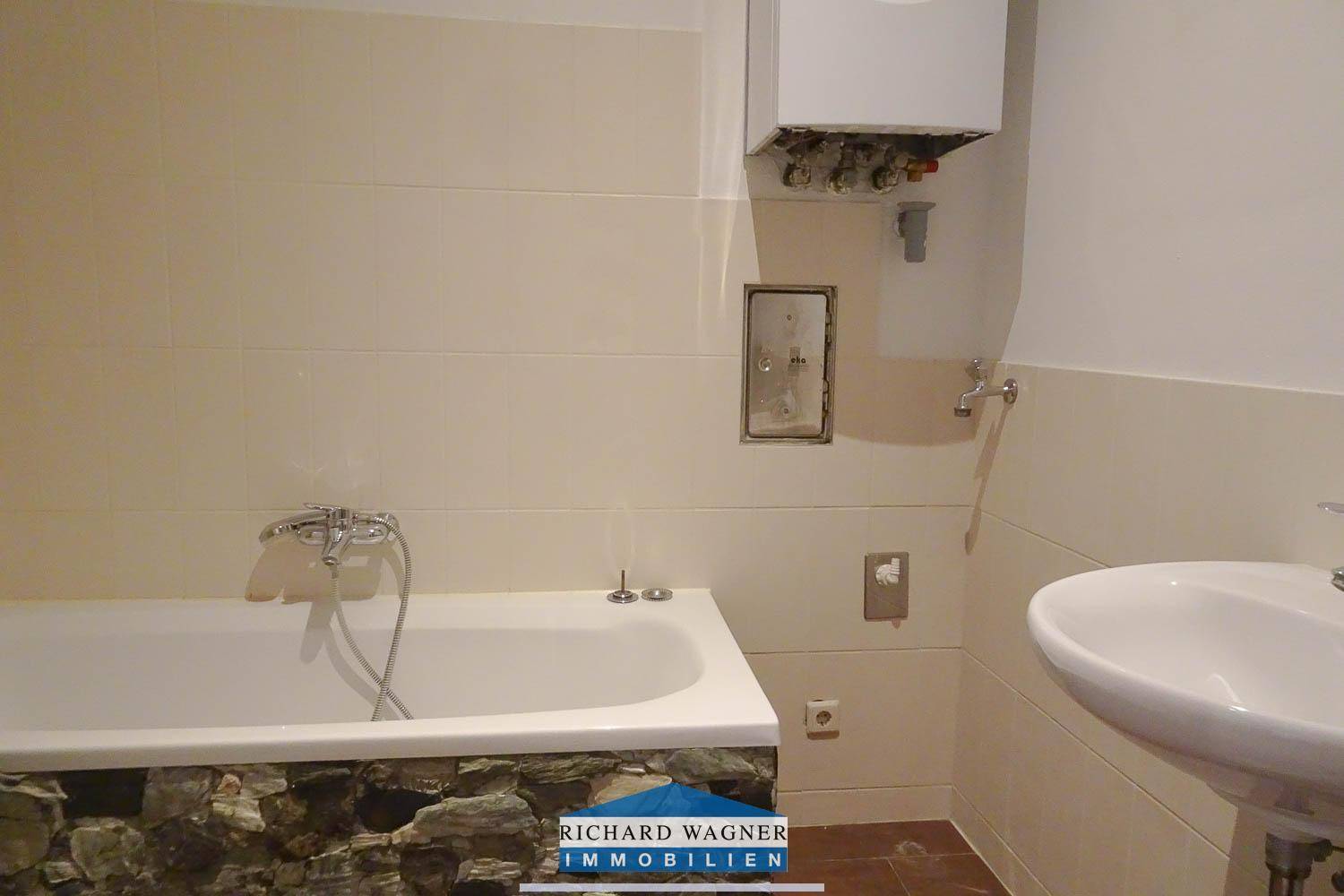 Badezimmer mit Badewanne, Waschbecken und Wandfliesen in hellem Beige, ausgestattet mit einem Boiler.
