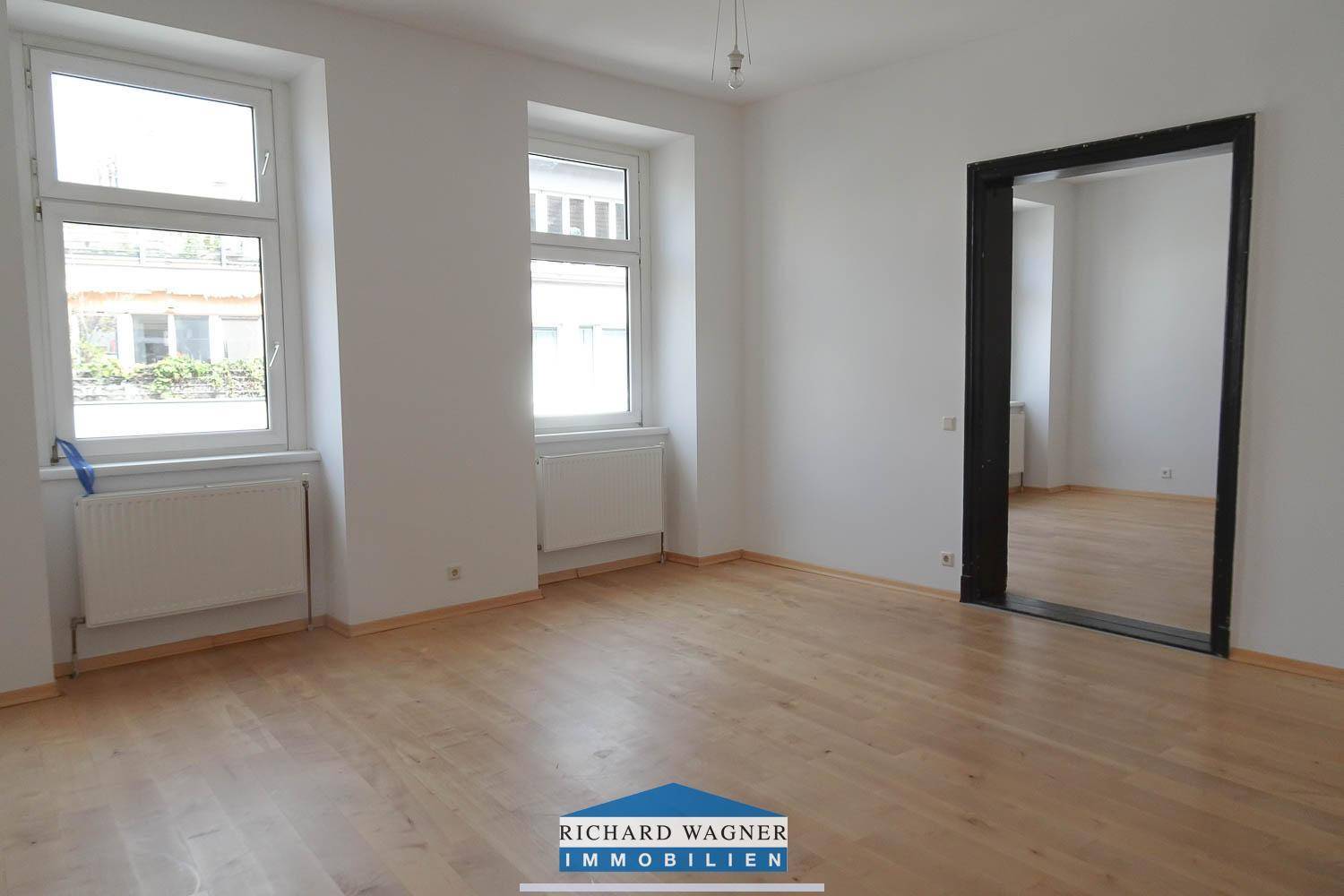 Geräumiges Zimmer mit Holzboden und zwei großen Fenstern, die viel Licht hereinlassen und eine angenehme Atmosphäre schaffen.