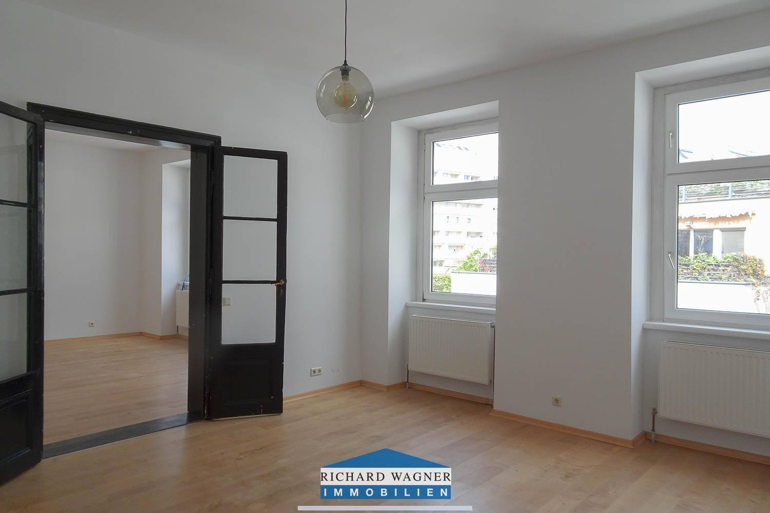 Helles Wohnzimmer mit Parkettboden, hohen Fenstern und Blick auf die Umgebung, ideal für natürliches Licht.