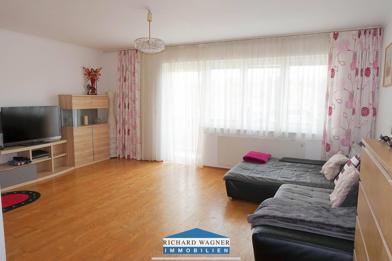Helles Wohnzimmer mit großem Fenster, bequemer Couch und warmem Holzfußboden.