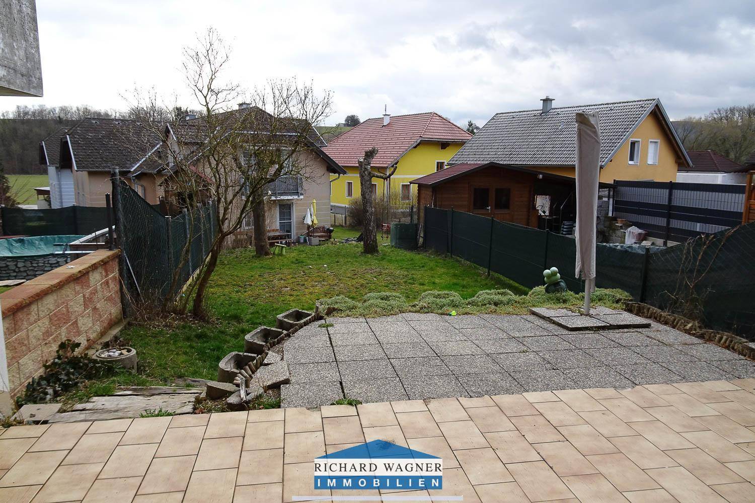 Gartenbereich mit gepflasterter Terrasse und Blick auf die umliegenden Häuser und Landschaft.