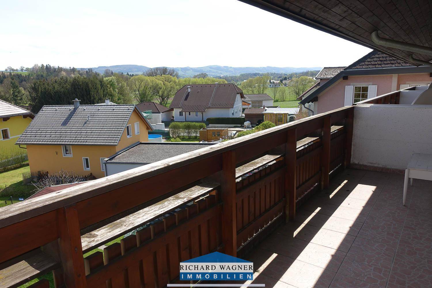 Geräumiger Balkon mit Fliesenboden und Holzgeländer, bietet weite Aussicht ins Grüne.