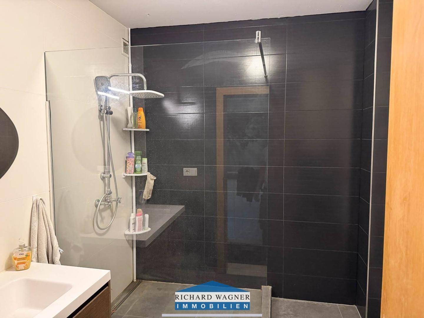 Modernes Badezimmer mit ebenerdiger Dusche und eleganten dunklen Fliesen.