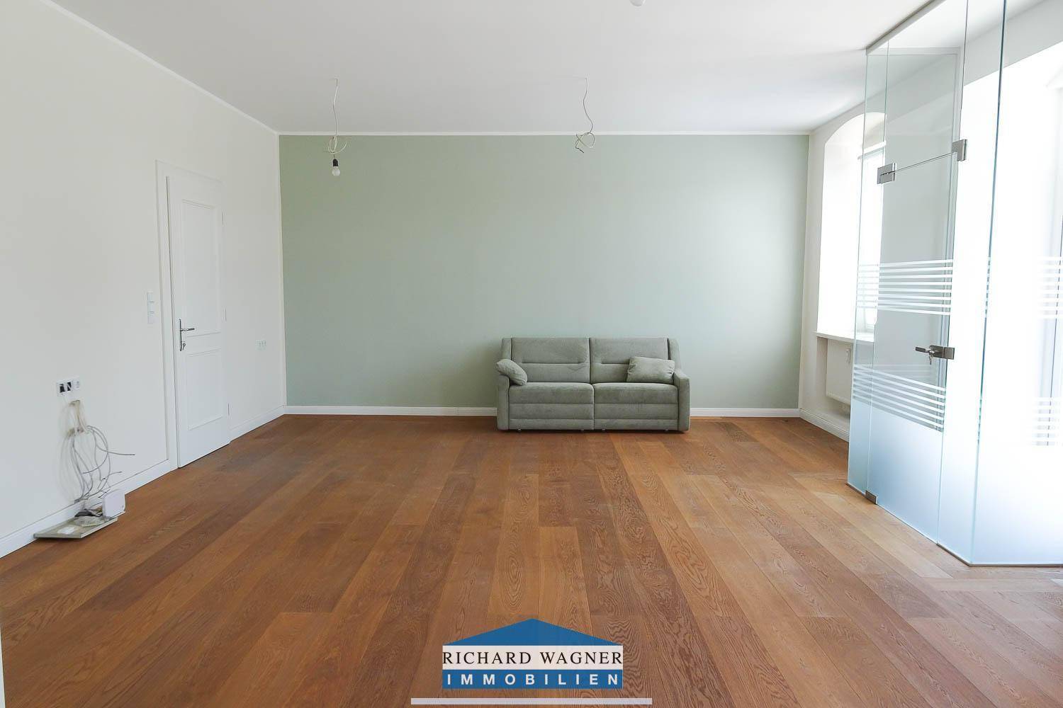 Helles Wohnzimmer mit Holzboden, einer Couch und einer hellgrünen Akzentwand.