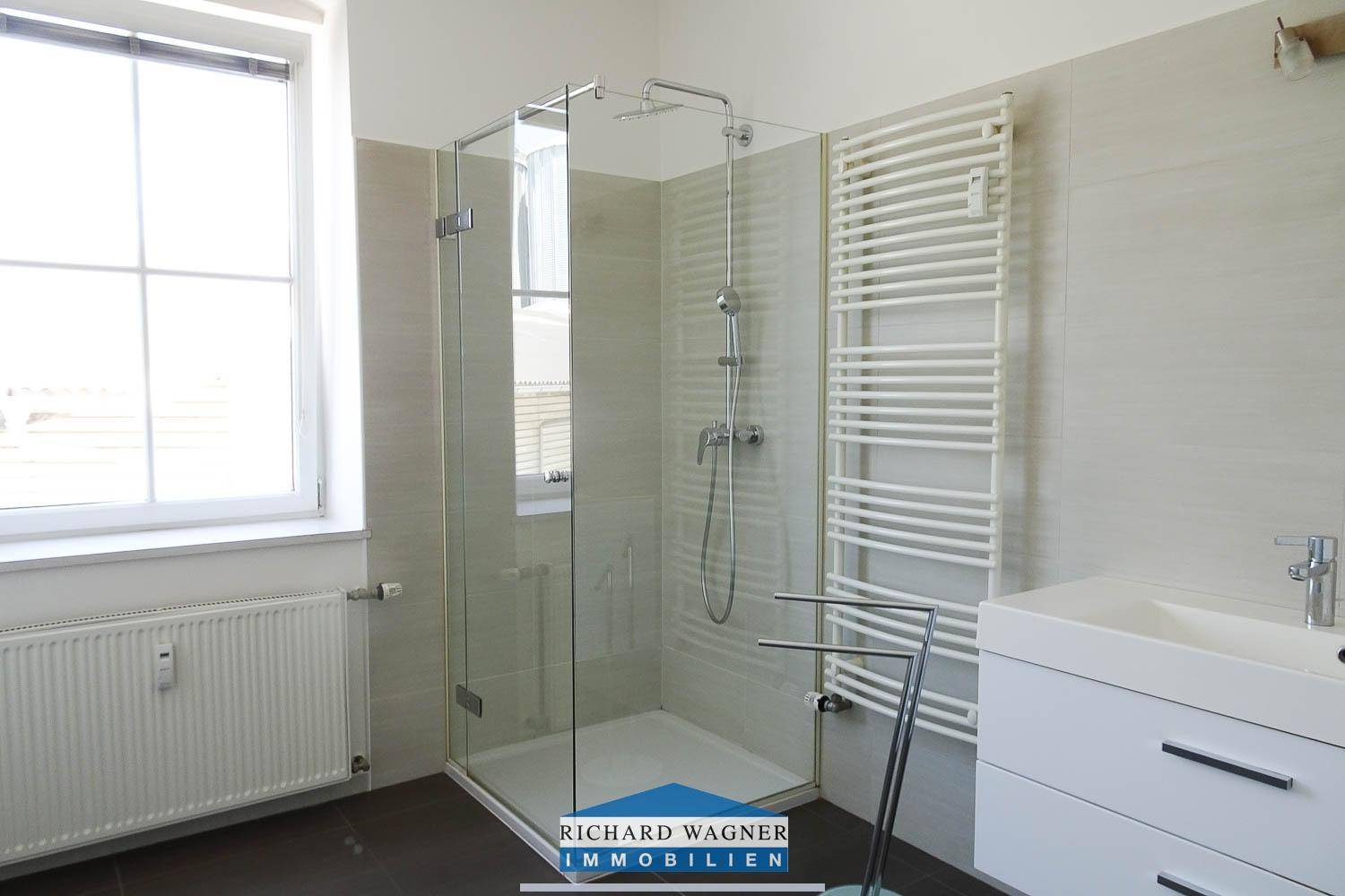 Modernes Badezimmer mit großer Glasdusche, beheiztem Handtuchhalter und Fenster.