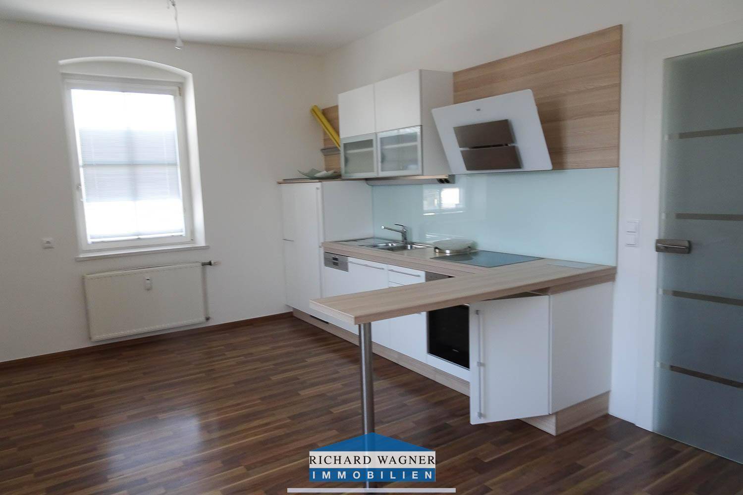 Helle Küche mit Laminatboden, weißen Schränken und integrierten Geräten.