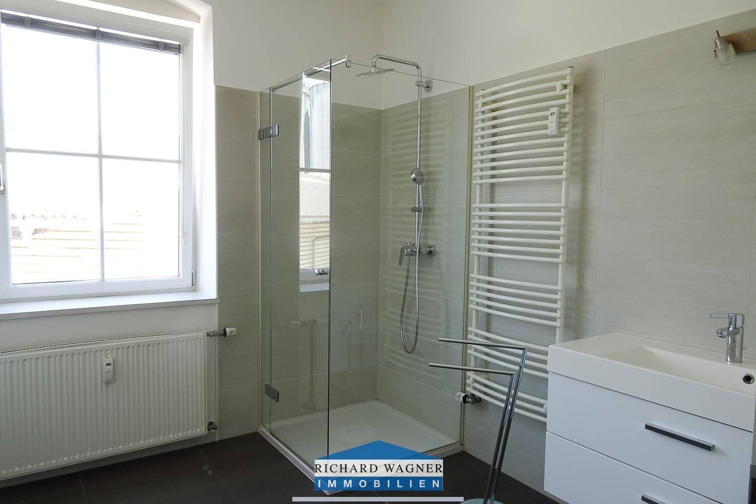 Helles Badezimmer mit begehbarer Dusche, Waschbecken und einem großen Fenster.