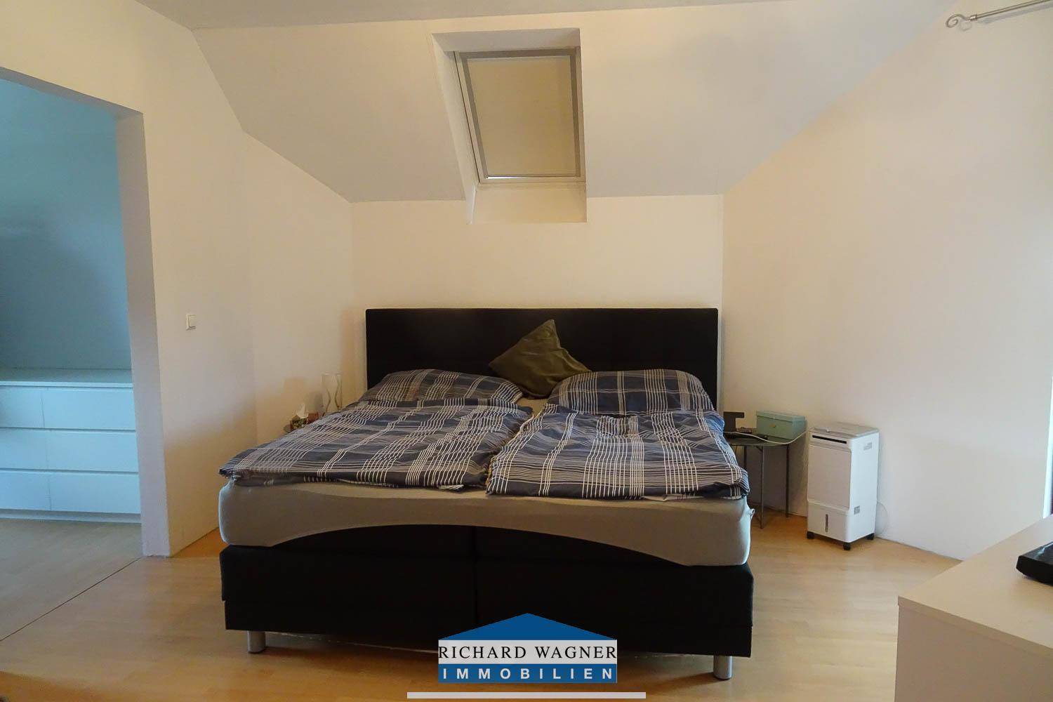 Helles Schlafzimmer im Dachgeschoss mit Doppelbett, Dachfenster und Holzboden.