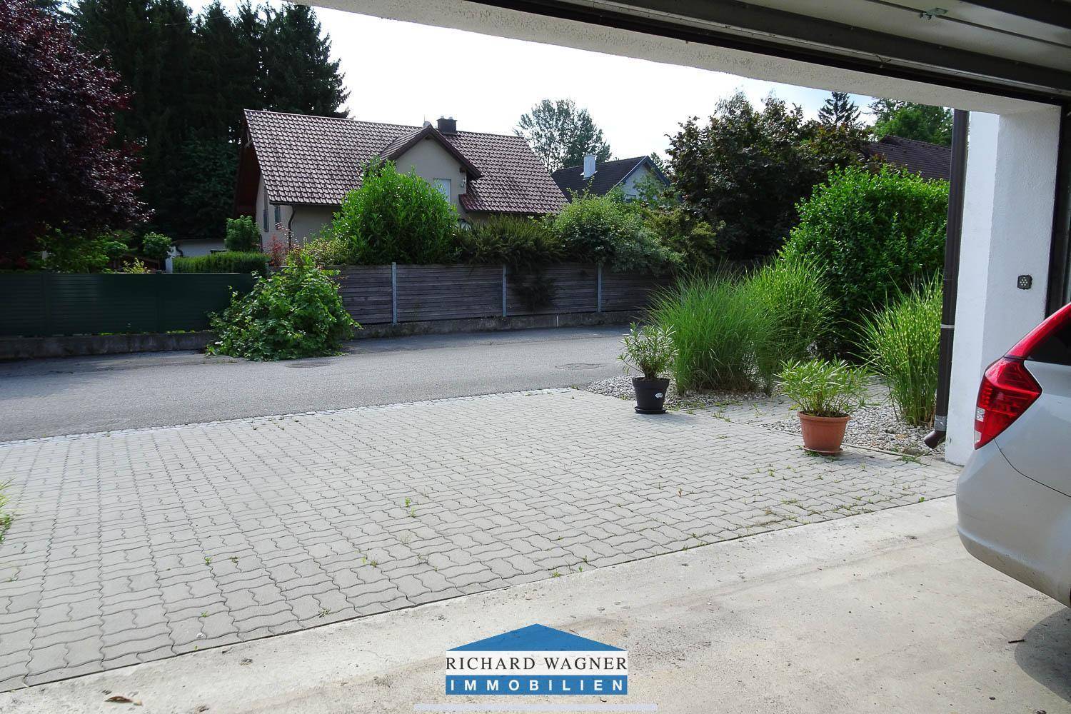 Gepflasterte Einfahrt vor der Garage mit Blick auf die ruhige Wohnstraße und umliegendes Grün.