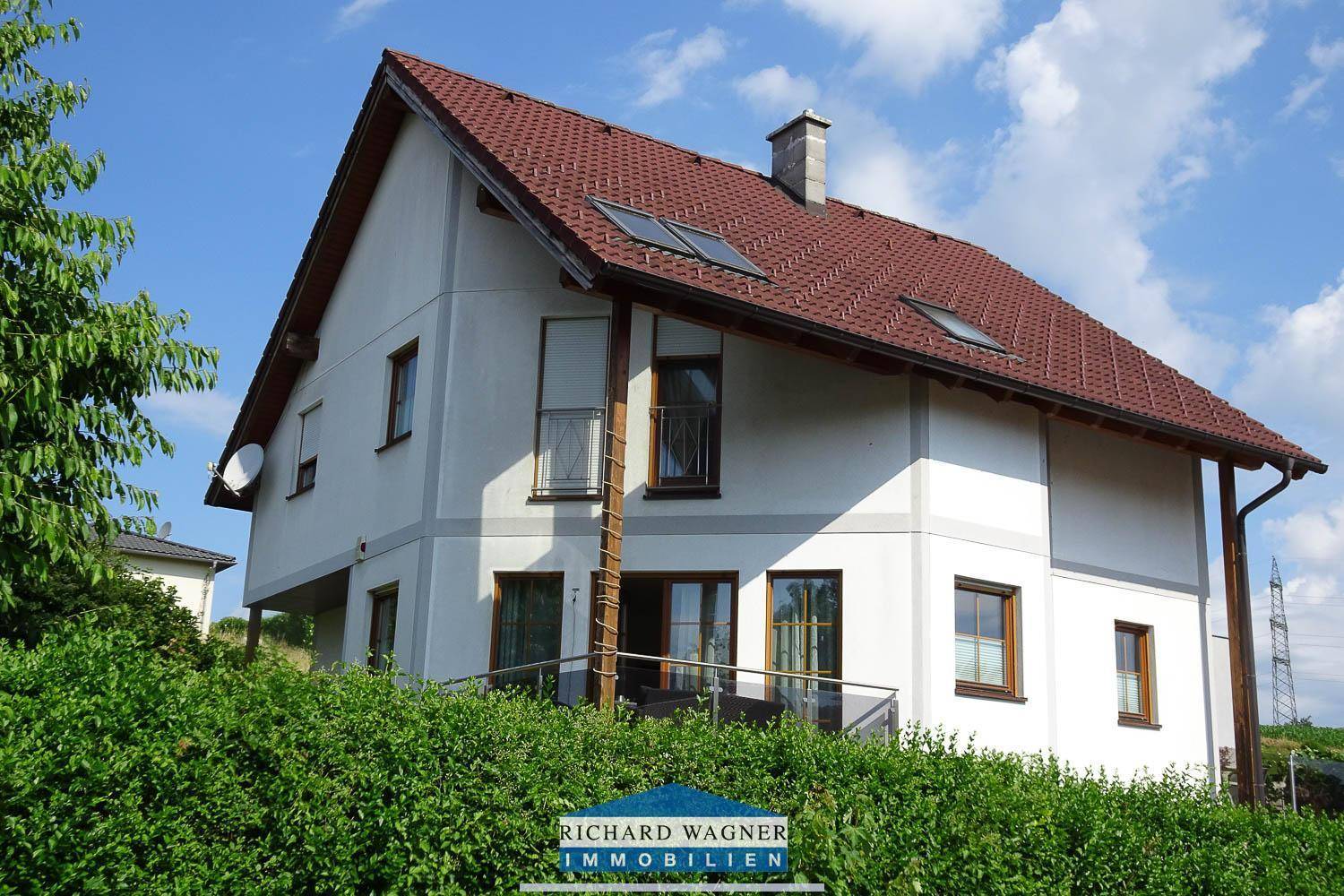 Seitenansicht des Hauses mit Satteldach, Dachfenstern und einem Balkon mit Glasgeländer.