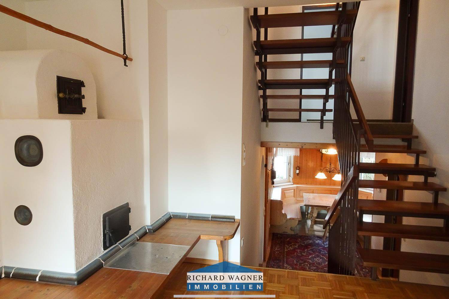 Blick auf den Kachelofen und die Holztreppe, die zum Essbereich im Untergeschoss führt.