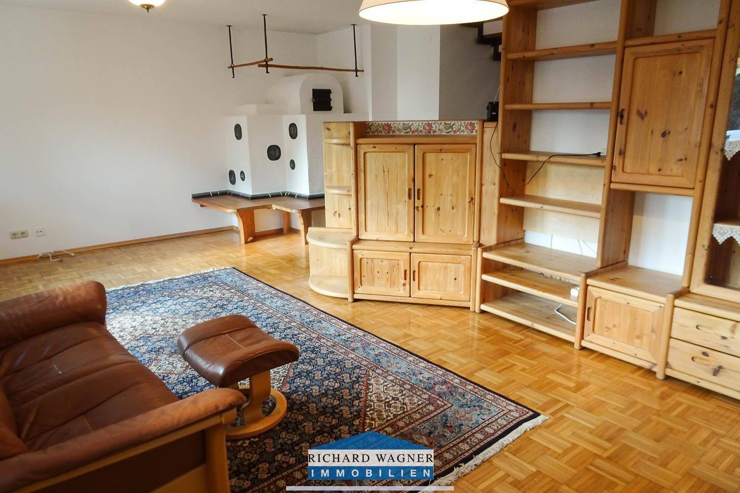 Geräumiges Wohnzimmer mit Parkettboden, einem traditionellen Kachelofen und Holzmöbeln.