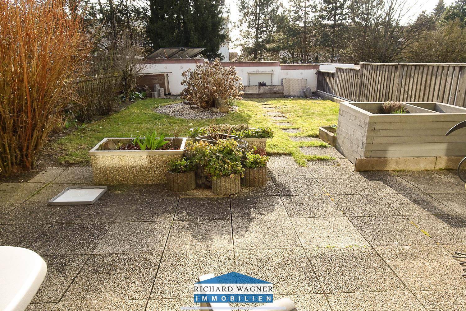 Gepflasterte Terrasse mit Blumenkübeln und angrenzendem Rasenbereich im Garten.