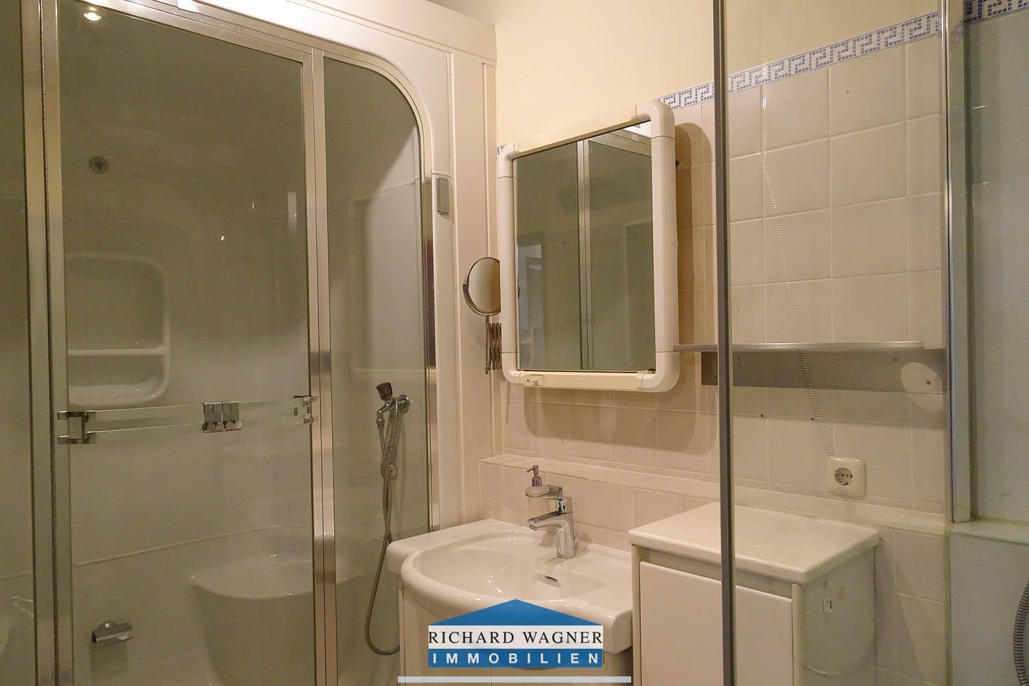 Helles Badezimmer mit Duschkabine, Waschbecken und weißen Fliesen im klassischen Stil.