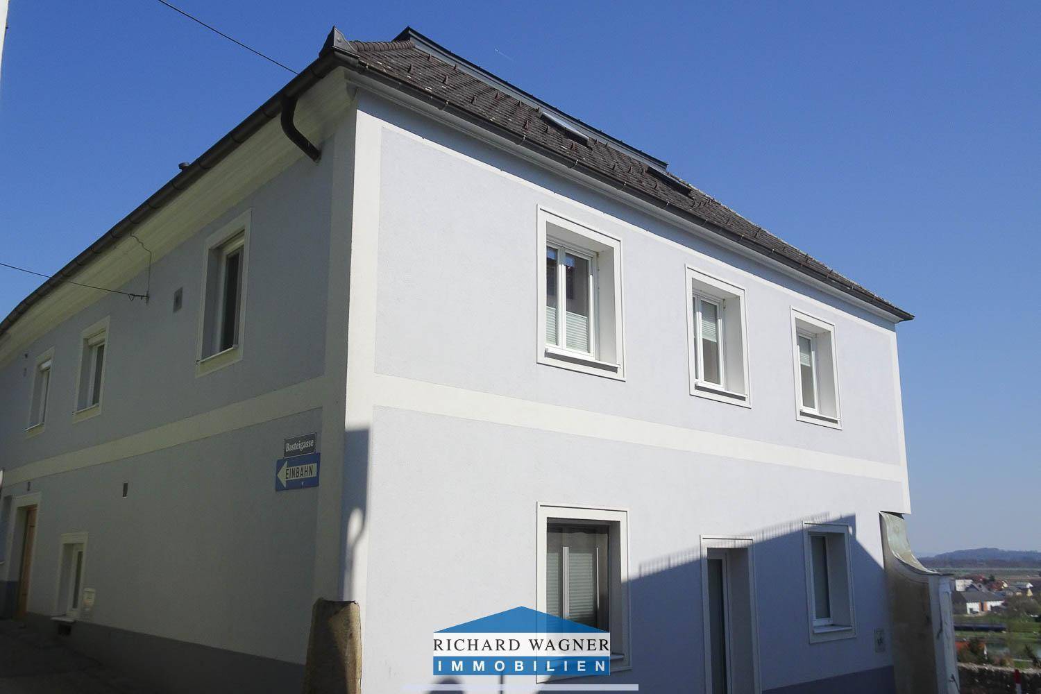 Seitenansicht eines hellblauen Gebäudes mit weißen Fensterrahmen und traditionellem Dach unter klarem Himmel.