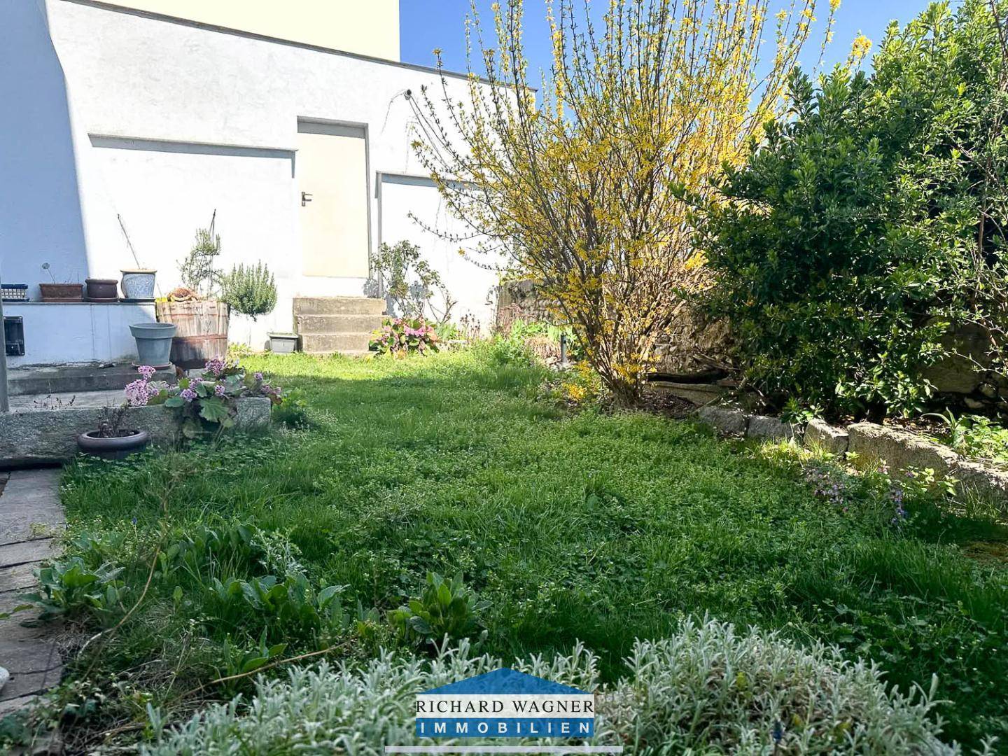 Gepflegter Gartenbereich mit Rasenfläche, blühenden Sträuchern und einer kleinen Terrasse.