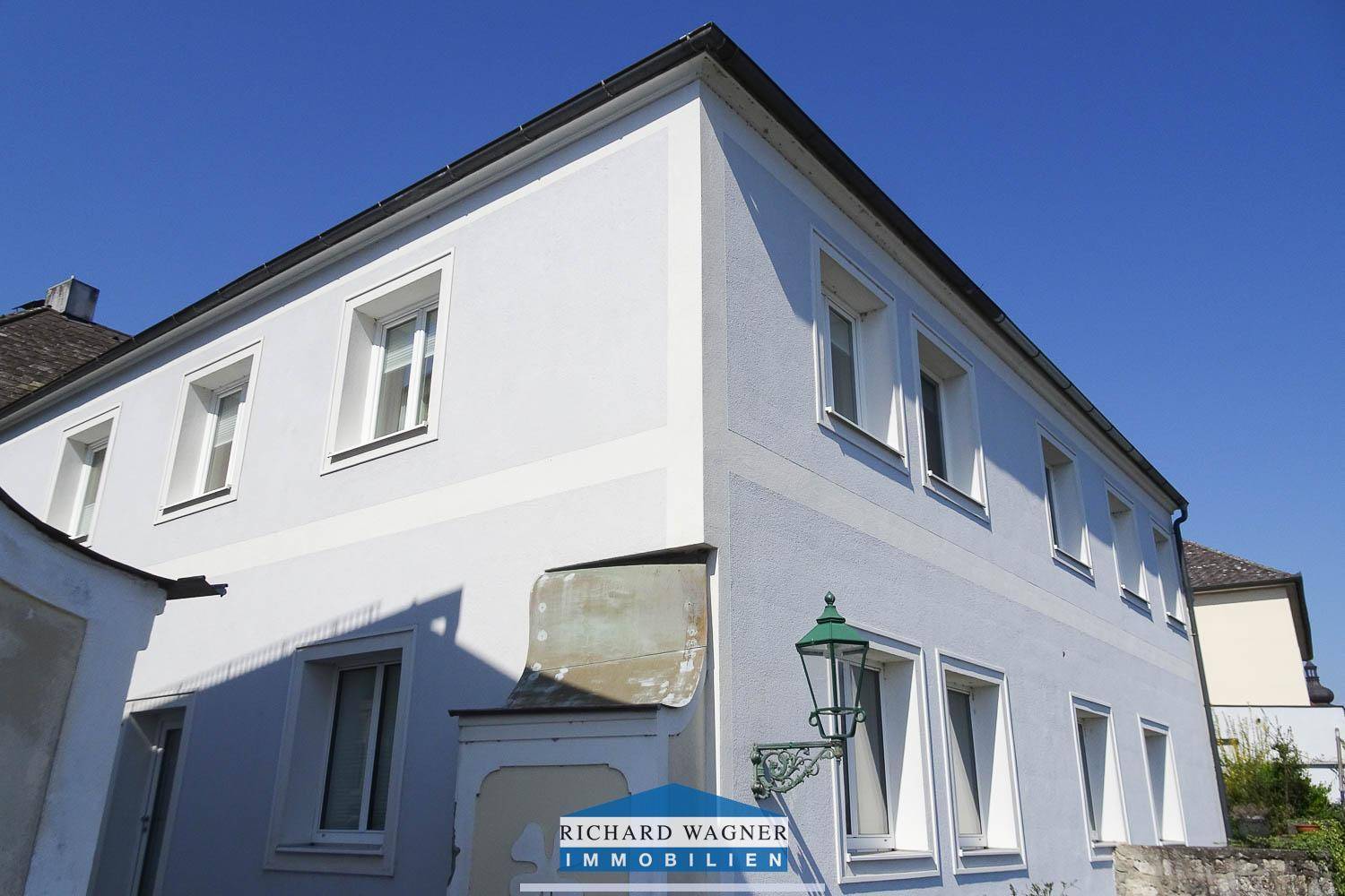 Eckansicht des Gebäudes mit hellblauer Fassade, weißen Fenstern und einer historischen Laterne.