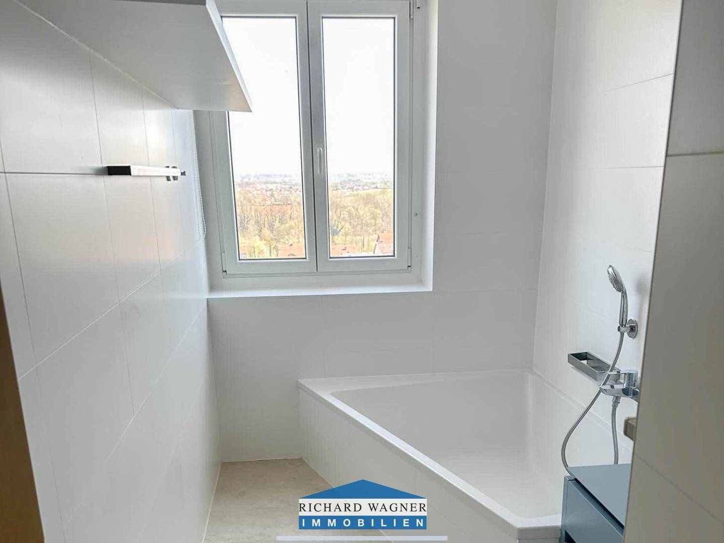 Helles Badezimmer mit weiß gefliesten Wänden, Badewanne und Fenster mit Weitblick.