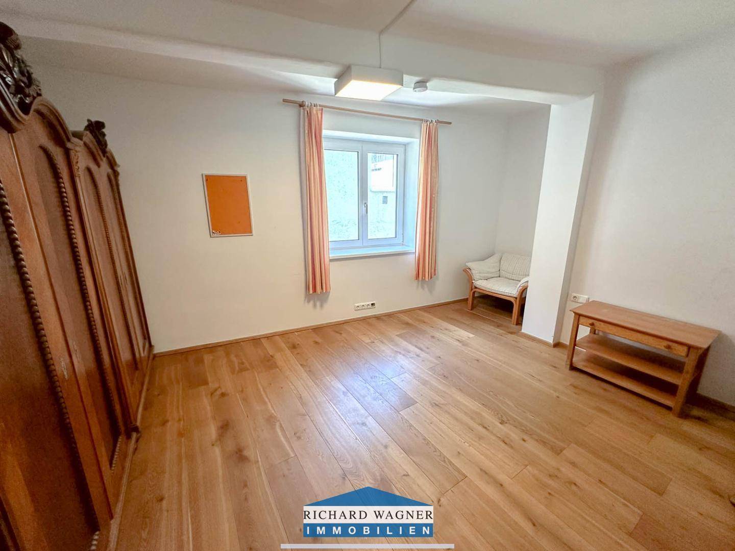 Helles Schlafzimmer mit Holzboden, großem Holzschrank und Fenster mit Blick nach draußen.