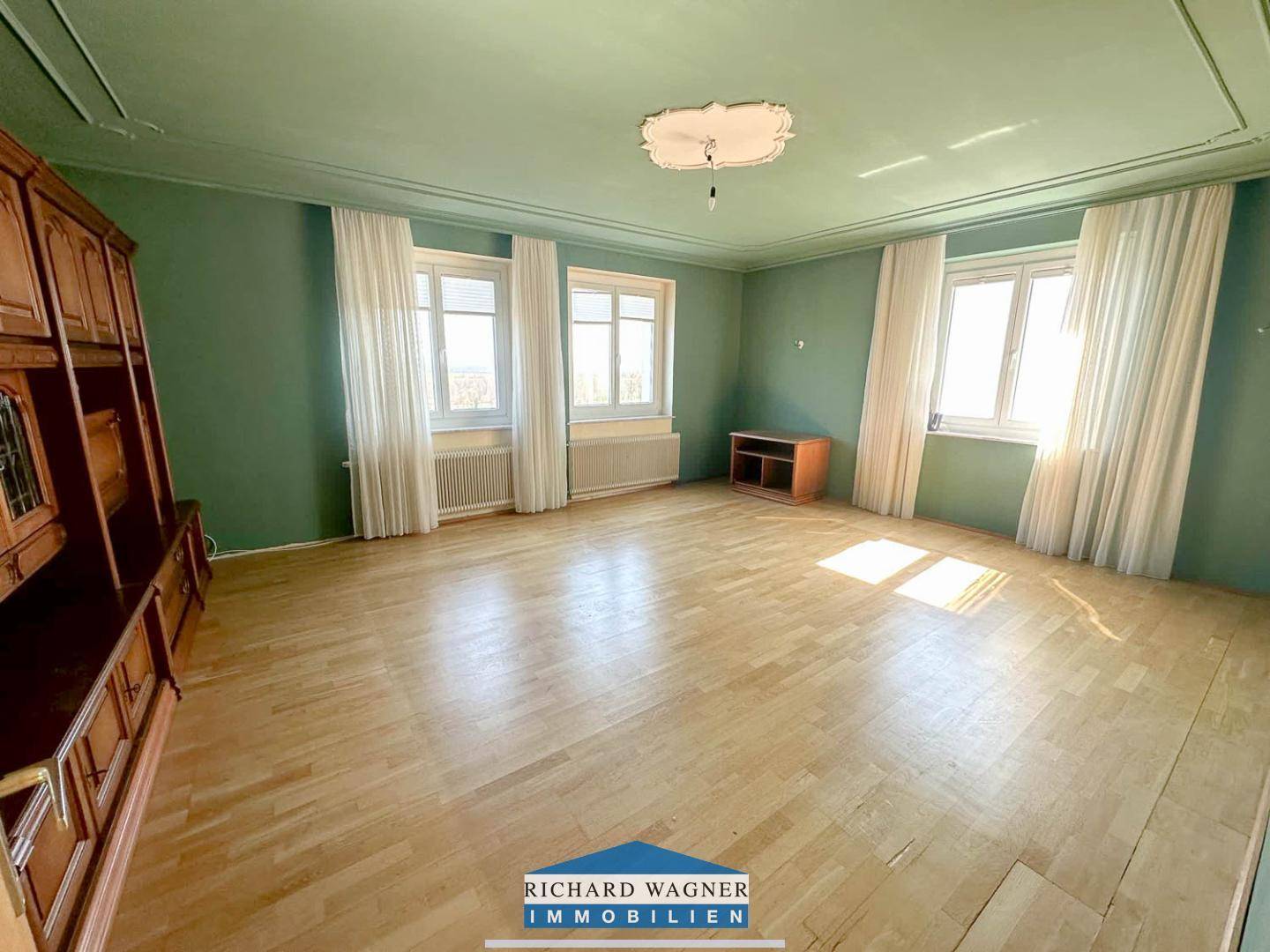 Geräumiges Wohnzimmer mit grün gestrichenen Wänden, Parkettboden und Stuckdecke.
