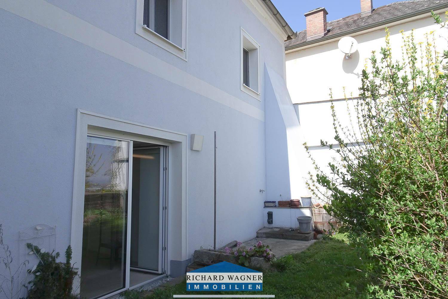 Hinterer Bereich des Hauses mit direktem Zugang zum kleinen Garten und grüner Bepflanzung.