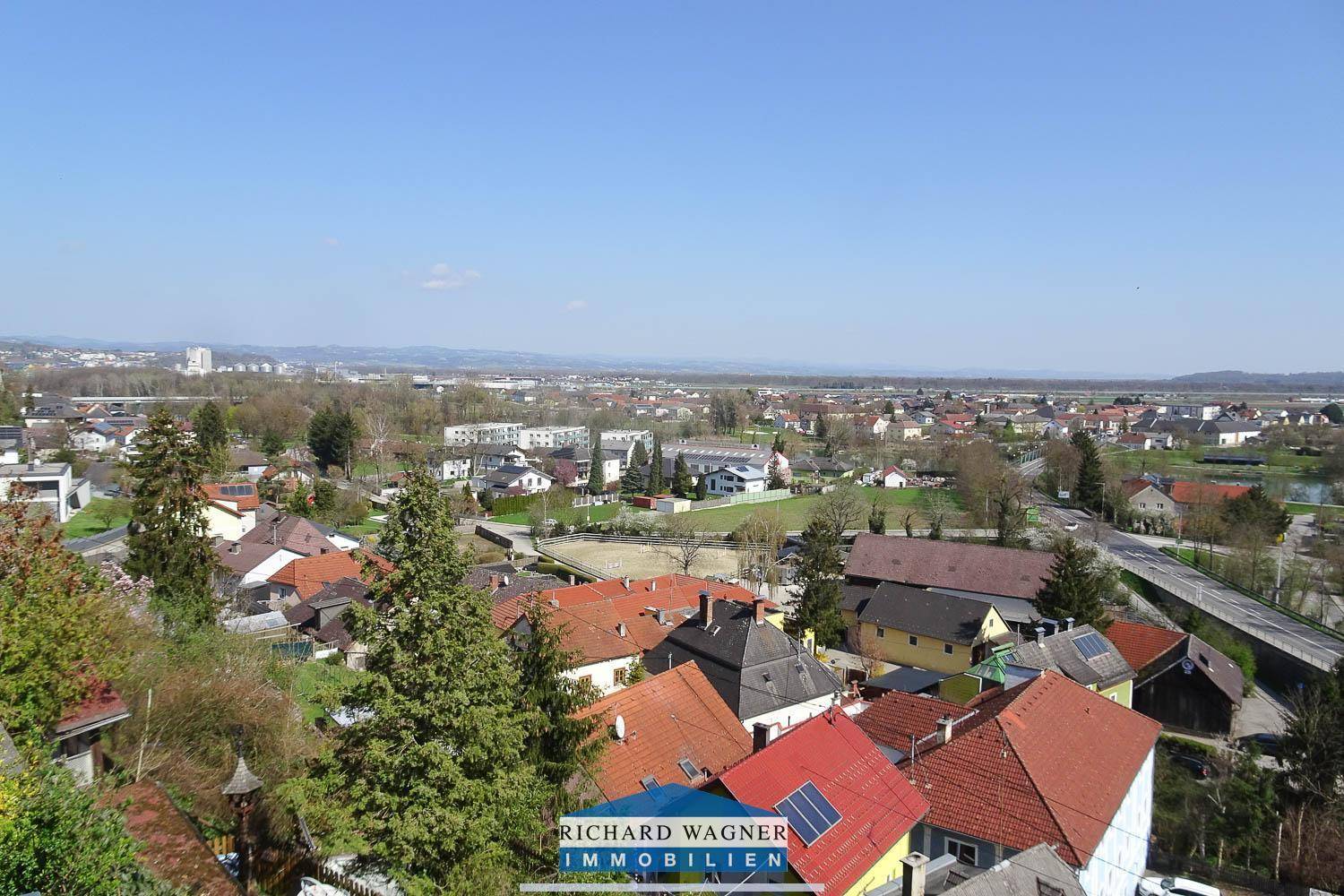 Weitläufiger Blick über eine Wohnsiedlung mit viel Grün und angrenzenden Feldern.