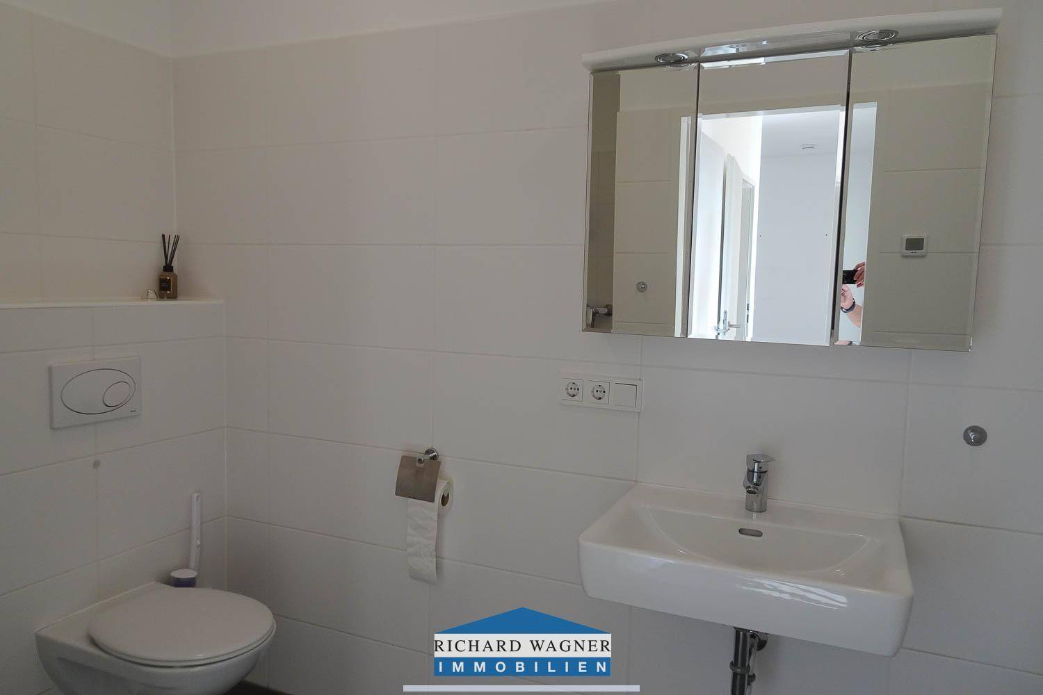 Modernes Badezimmer mit weißen Fliesen, wandhängendem WC, Einzelwaschbecken und Spiegelschrank.