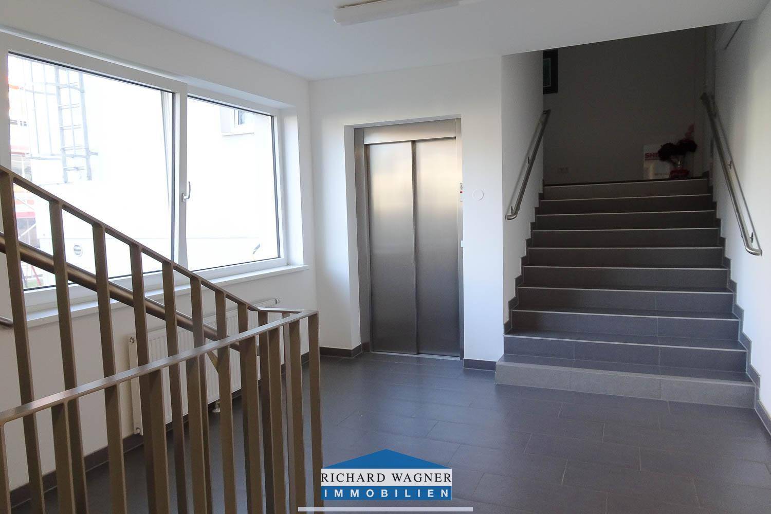 Heller Treppenhausbereich mit Aufzug und breiter Treppe, bietet bequemen Zugang zu den Etagen.