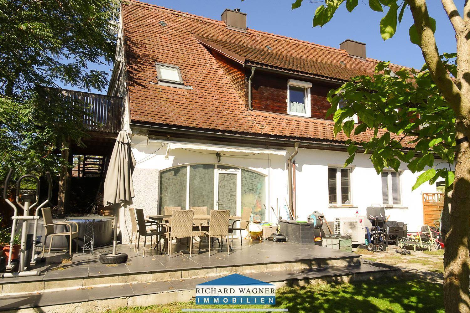 Terrasse mit Gartenmöbeln und Sonnenschirm, angrenzend an das Haus mit Balkon.
