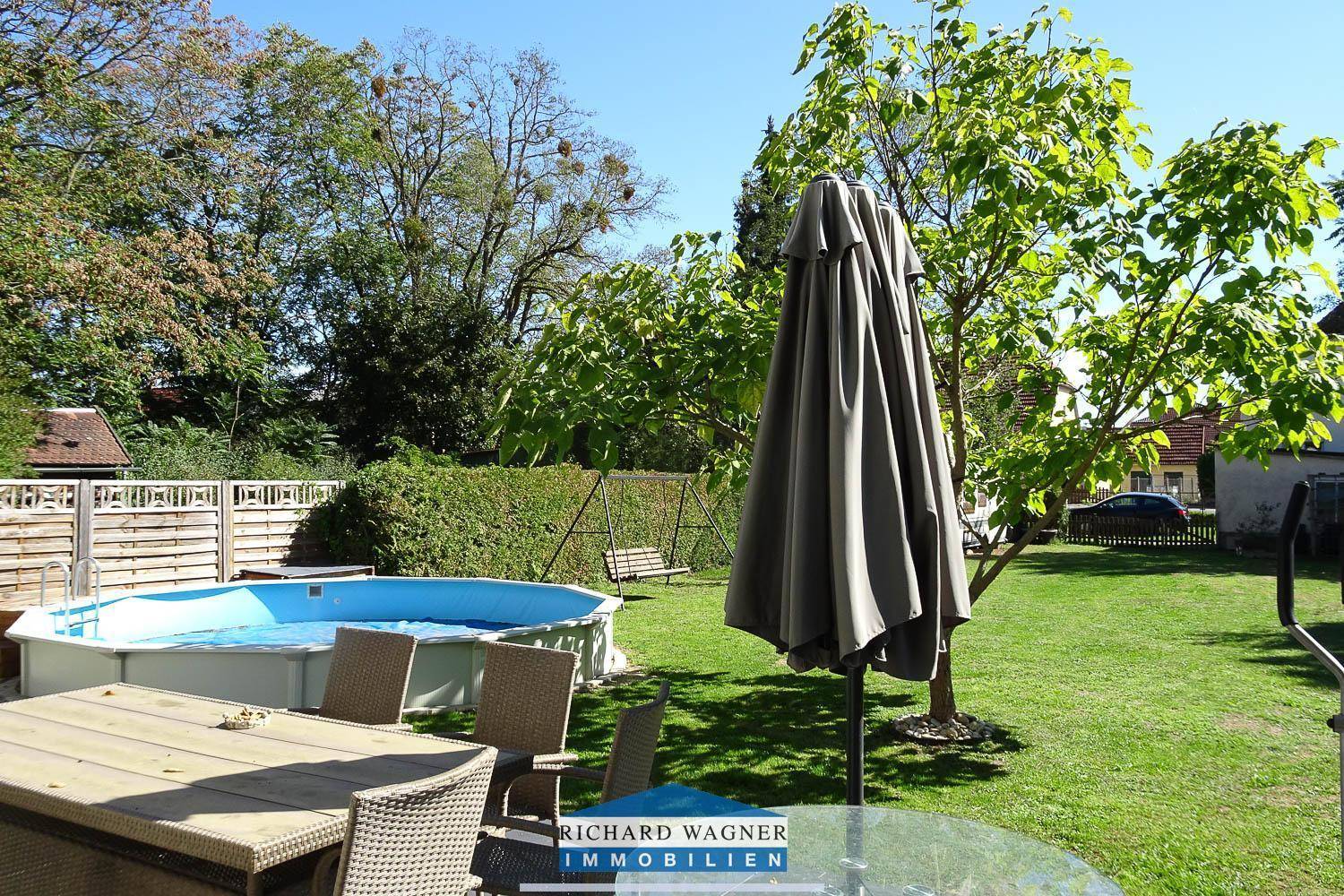 Sonniger Gartenbereich mit Aufstellpool, Sitzgelegenheiten und viel Grün.