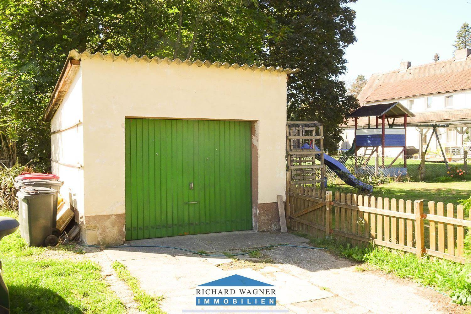 Freistehende Garage mit grünem Tor und einem Spielplatz im Hintergrund des Gartens.
