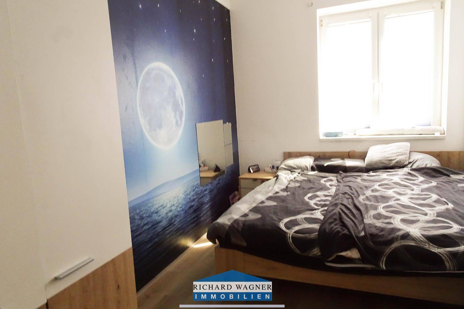 Schlafzimmer mit Doppelbett, Nachttischen und einer Mond-Wandtapete.