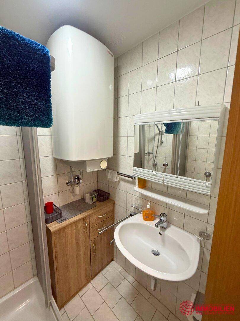 Badezimmer mit Waschbecken, Spiegelschrank und Fliesen an Wänden und Boden.