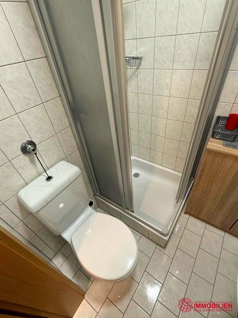 Badezimmer mit Toilette und Duschkabine, komplett gefliest.