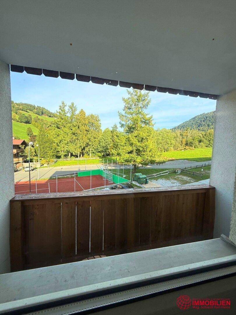 Balkon mit weitem Blick auf einen Tennisplatz und die umliegende grüne Landschaft.